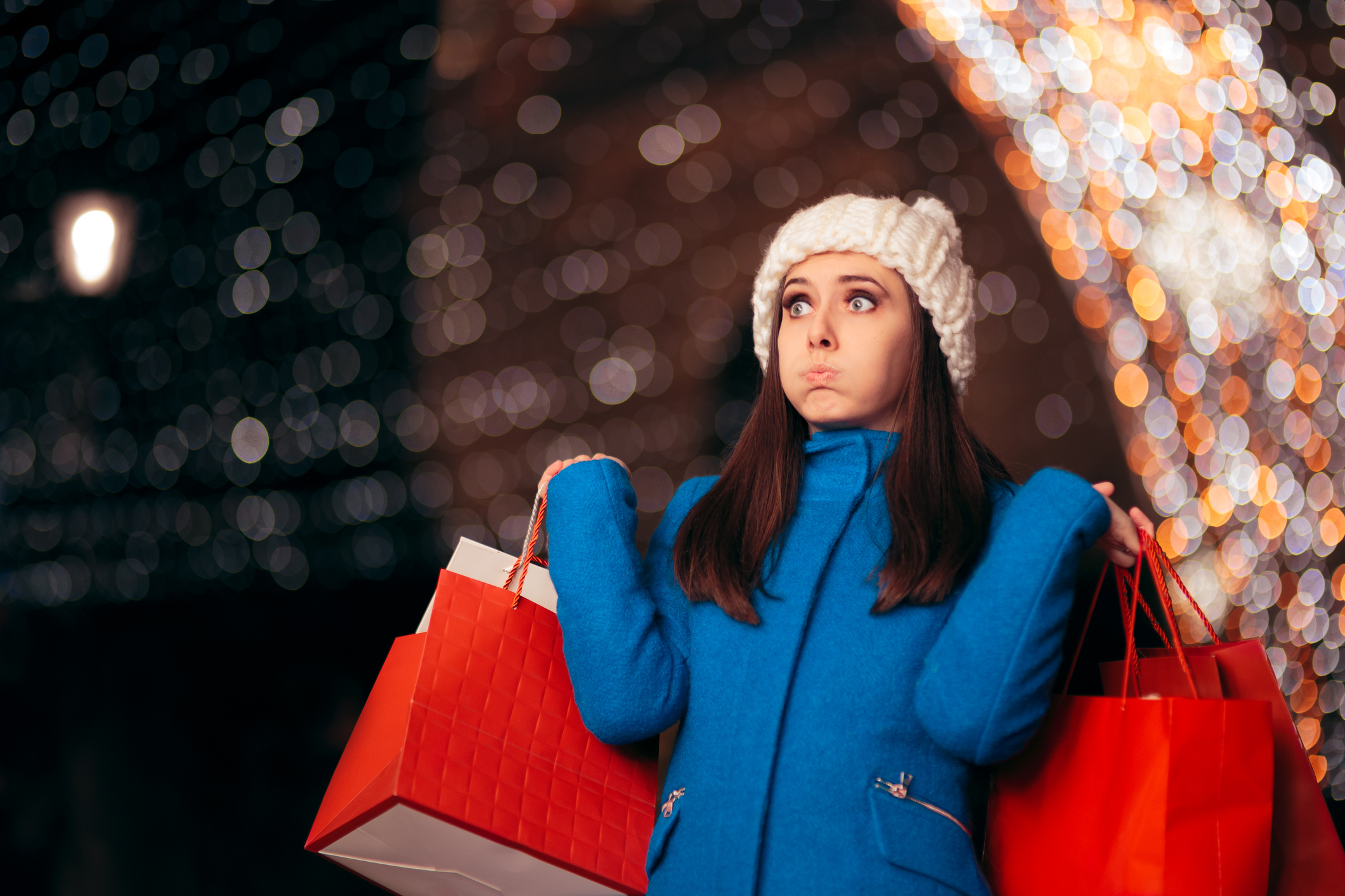 Tired girl holding shopping bags amid Christmas lights décor