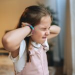 Girl covering her ears to block loud winter house noises indoors