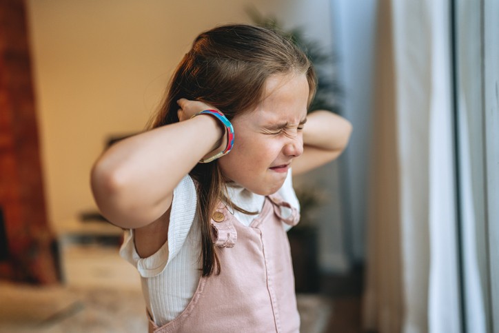 Girl covering her ears to block loud winter house noises indoors